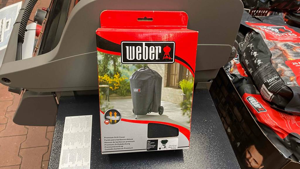 Auf einer dunklen Fläche steht eine getestete Grillabdeckung in Originalverpackung.