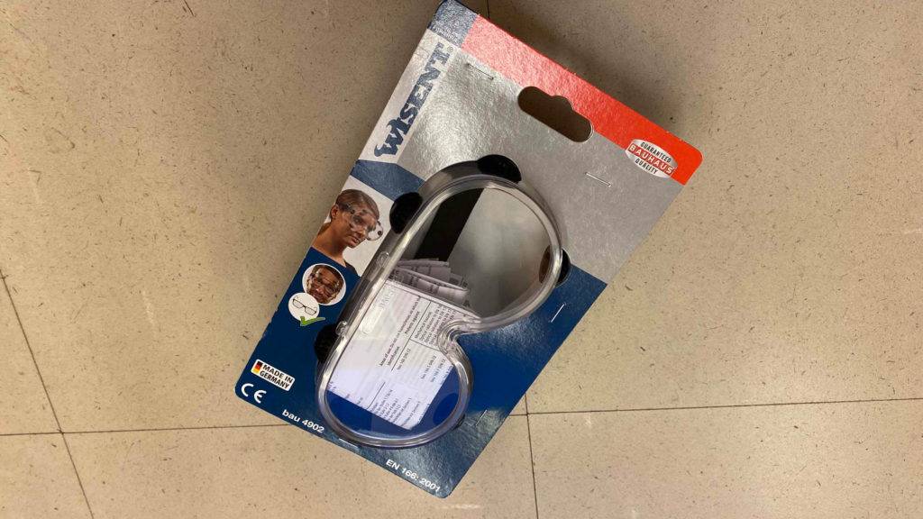 Schutzbrille getestet: Eine Brille in Originalverpackung quer auf Fließenboden