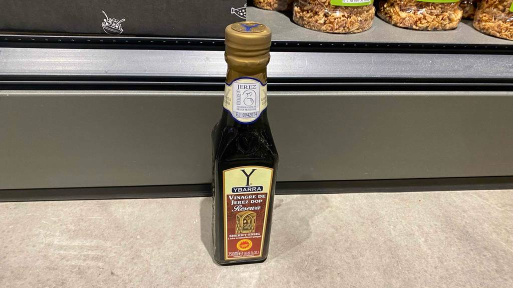 Eine getestete Flasche Sherryessig steht vor einem Regal auf einem hellen Boden.