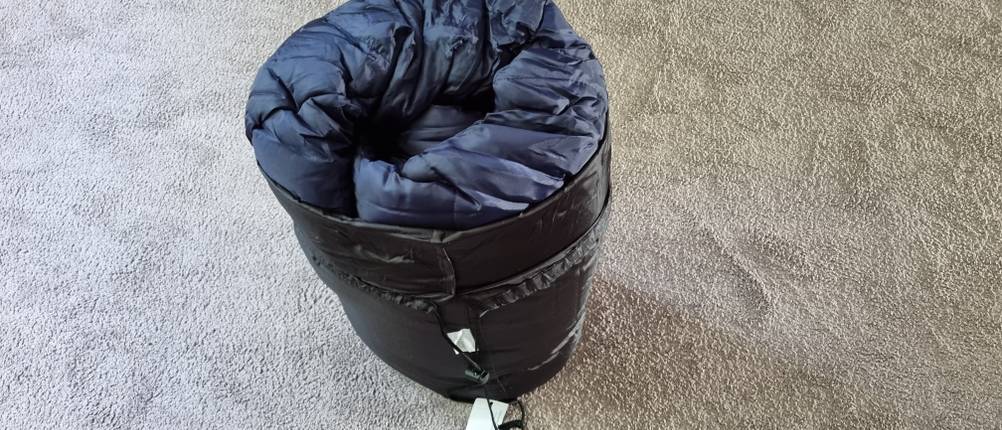 Schlafsack-Test: Ein dunkelblauer, eingerollter Schlafsack steht auf dem Boden. 