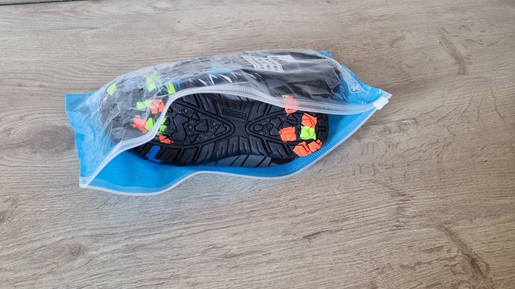 Ein schwarzes Pärchen Badeschuhe in einer durchsichtigen Verpackung. 