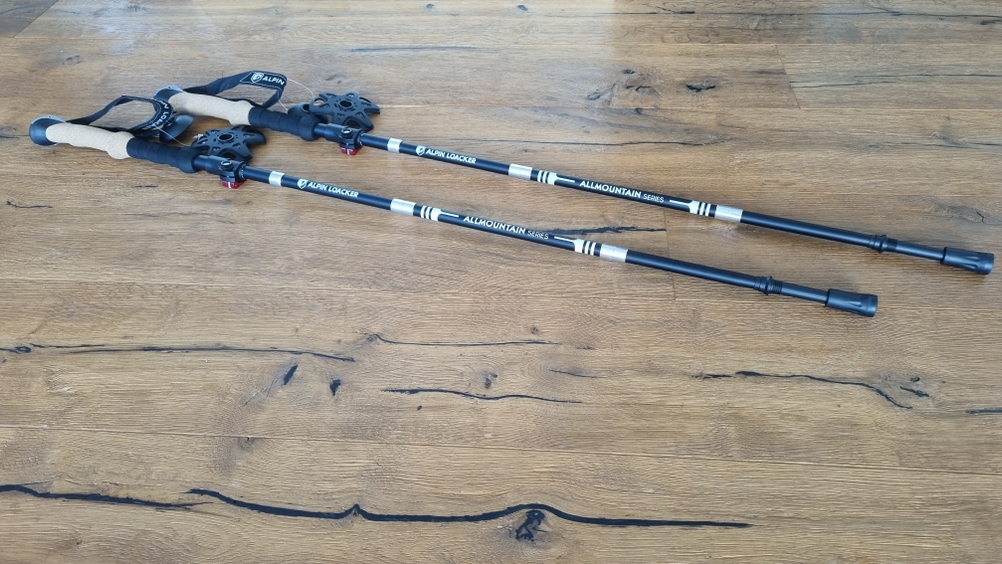 Zwei schwarze Wanderstöcke liegen nebenaneinander auf dem Boden. 