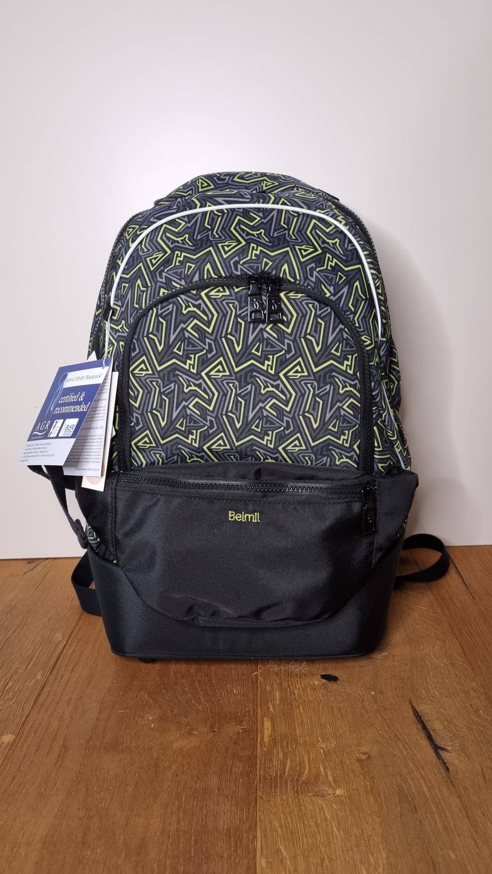 Ein dunkler, getesteter Schulrucksack mit gelblichen Streifenmustern stehend auf Holzboden.
