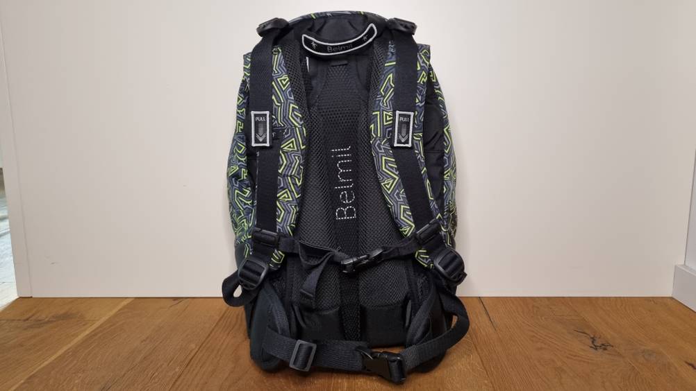 Die Rückseite eines Schulrucksackes im Test mit dem Gurtsystem stehend auf Holzboden.