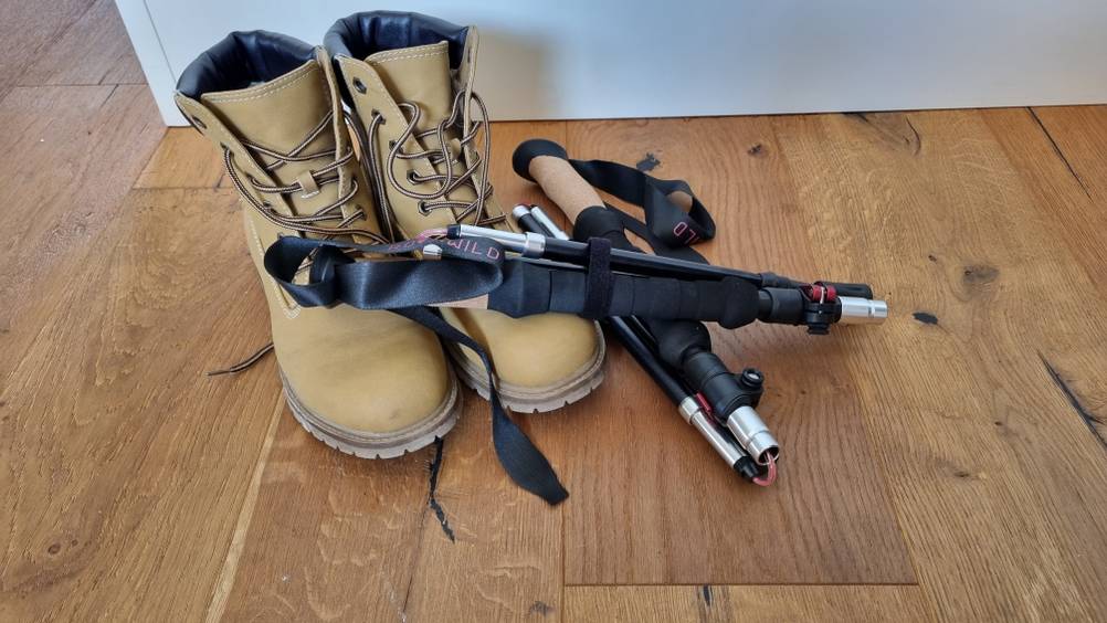 Ein zusammengefaltetes Pärchen Trekkingstöcke neben einem Paar Wanderschuhe. 