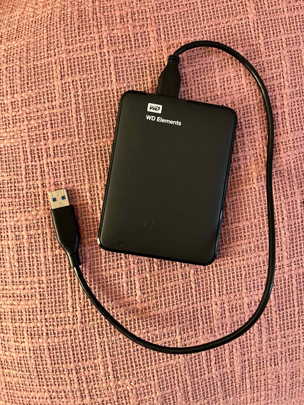 Externe-Festplatte-1tb im Test: Eine Festplatte mit Kabel liegt auf einem rosa Stoff