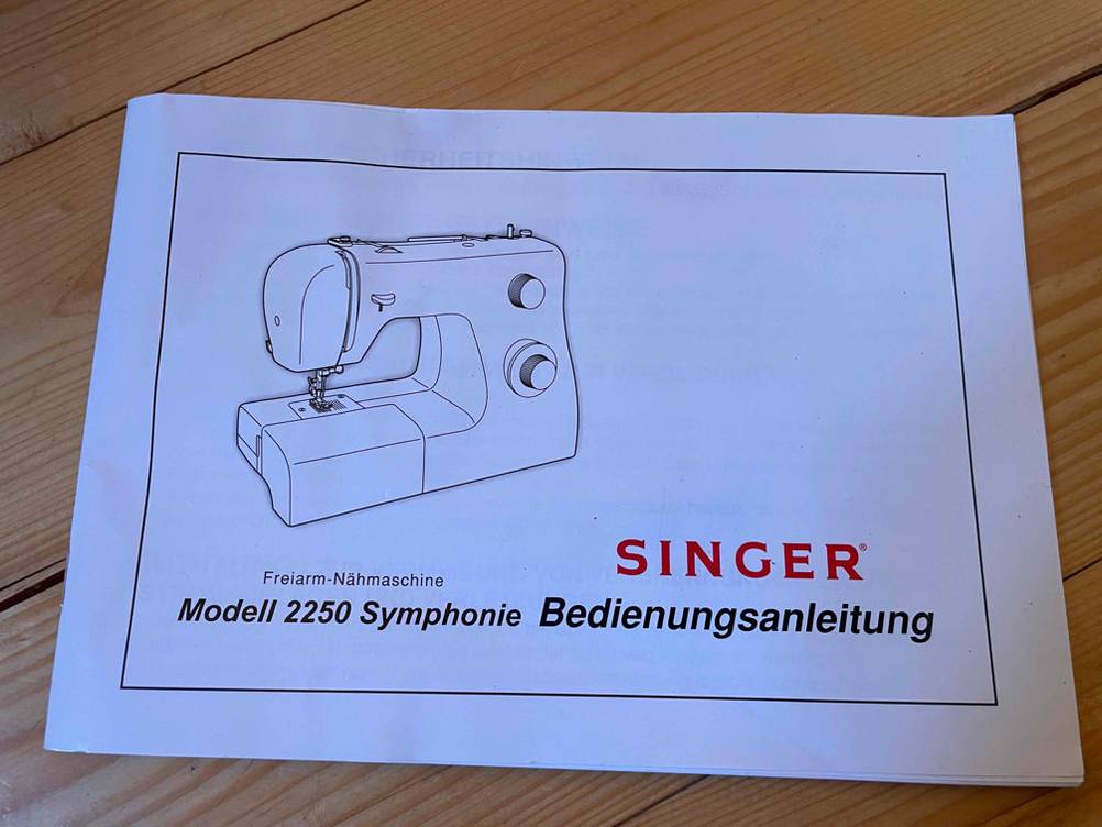 Die Bedienungsanleitung einer getesteten Singer Nähmaschine liegt auf einem Boden.