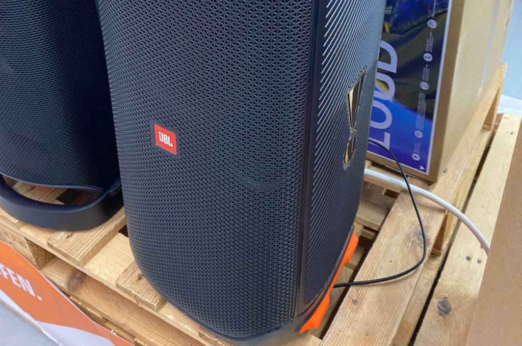 Eine getestete Musikbox steht neben einer anderen auf einer Holzpalette.