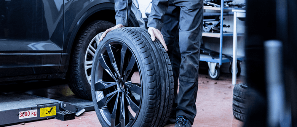 165/60-R14-Ganzjahresreifen im Test: Autoreifen wird in einer Werkstatt von einem Mann gehalten.