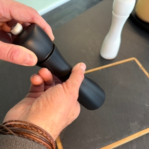 Eine Hand dreht an der Pfeffermühle vom Peugeot 2/24277 Tahiti Duo.