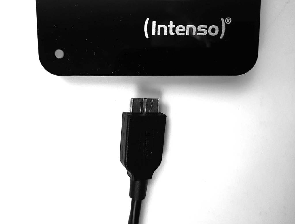 Detailansicht des USB-Steckers, der vor einer getesteten Intenso externen Festplatte liegt.