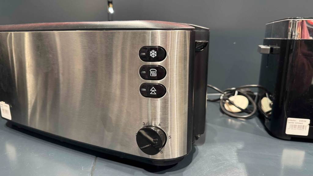 Der getestete Doppel-Langschlitztoaster aus Edelstahl steht neben einem schwarzen Toaster auf einem grauen Verkaufsregal.