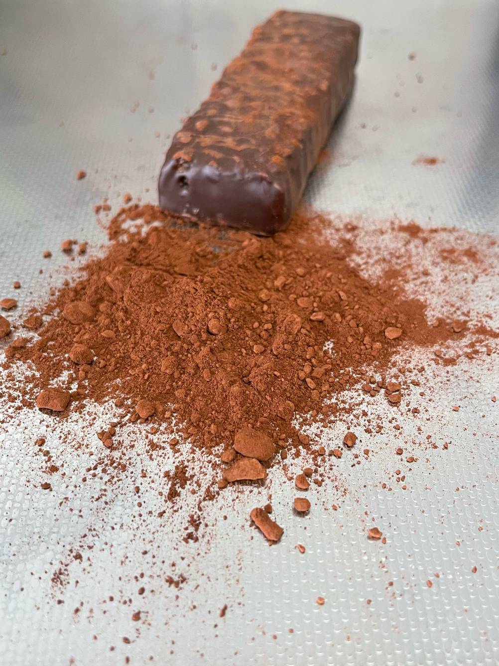 Der getestete Weider-Proteinriegel ist auf einer Fläche platziert, worauf sich ausgetreuter Kakao befindet.