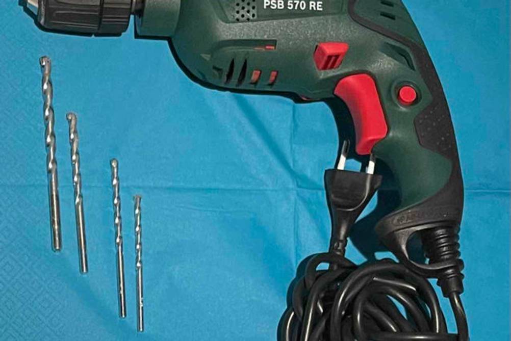 Bohrer-Set-Test: verschiedene Bohrer, und elektrisch betriebenes Bosch-Bohrgerät auf blauem Untergrund.