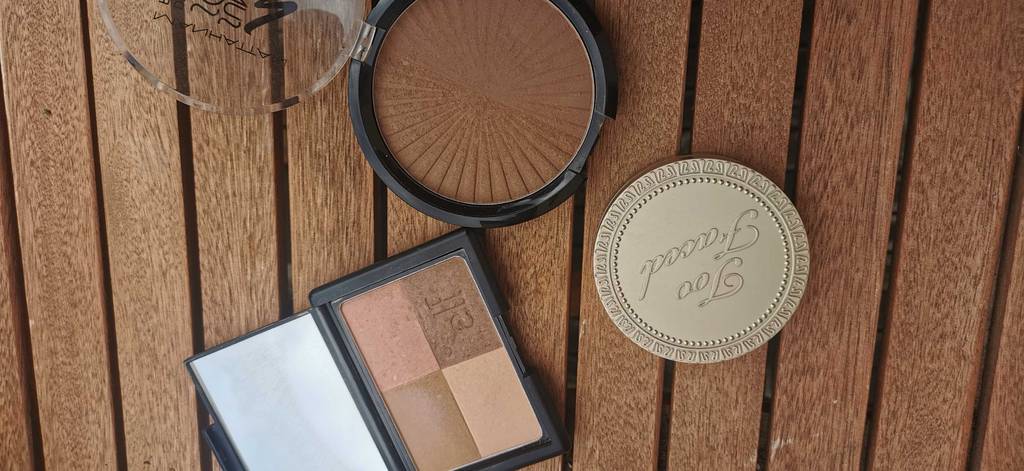 Bronzer im Test: 3 Bronzer, davon 2 geöffnet, liegen auf einem Holztisch.