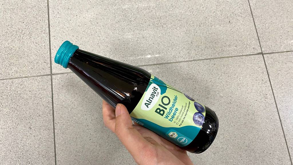 Heidelbeersaft im Test: eine Hand hält eine Flasche vor beige Oberfläche