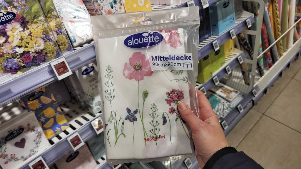 Die getestete Papiertischdecke wird vor einem Regal in der Hand gehalten.