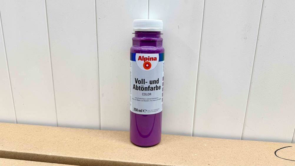 Abtönfarbe-Test: Die lilafarbige Abtönfarbe steht vor einer Wand.