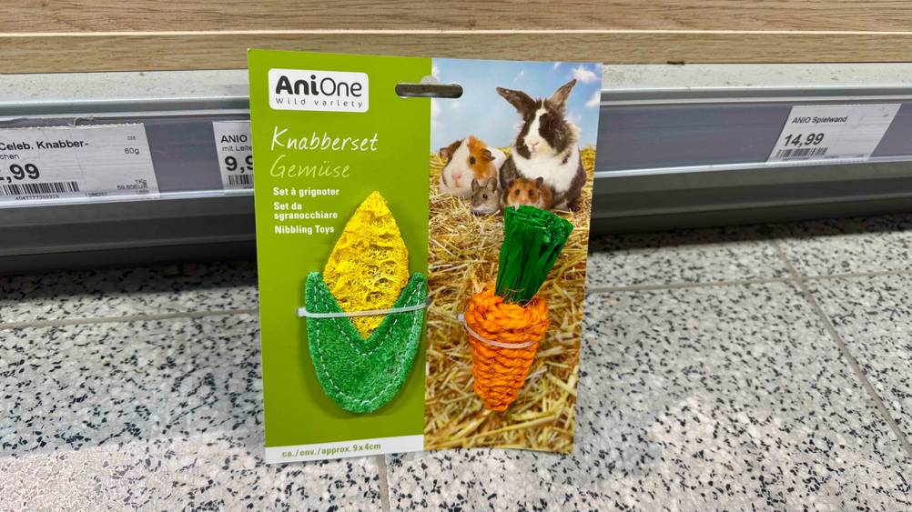 Das getestete Kaninchen-Spielzeug in Form von einem Maiskolben und einer Karotte ist an einem Regal angelehnt.