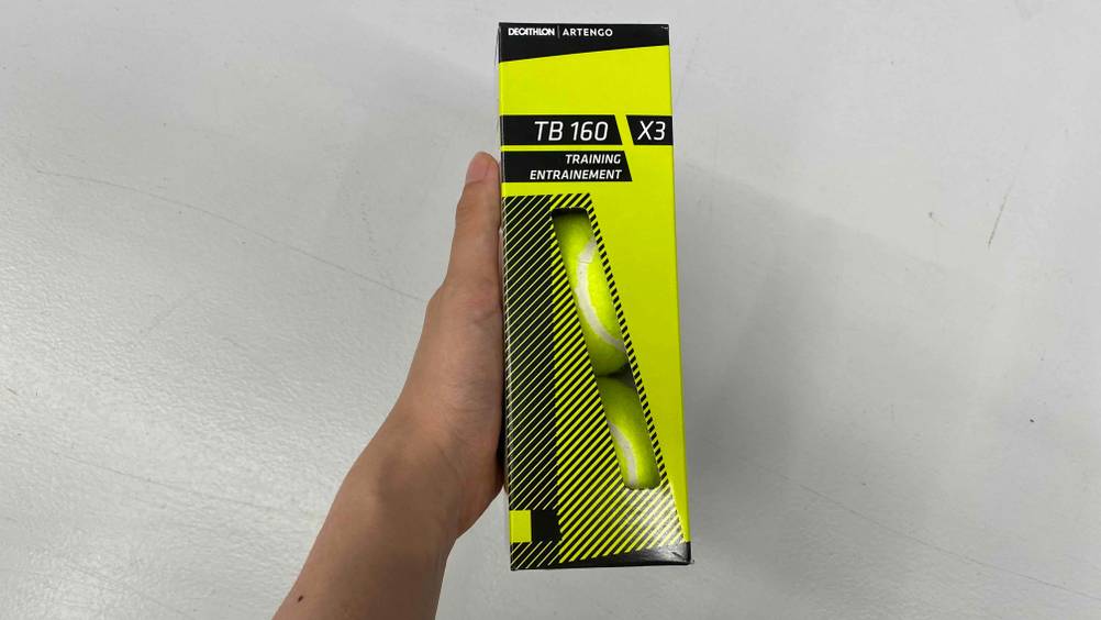 Tennisbälle im Test: Eine Hand hält eine Packung vor eine weiße Wand