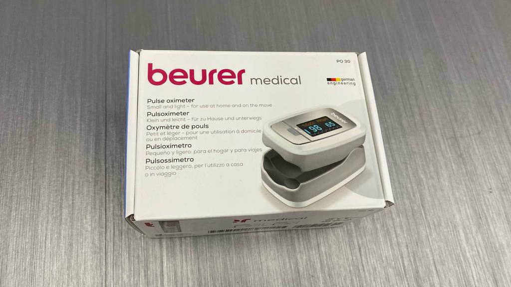 Auf einem grauen Boden liegt ein getestetes Pulsoximeter in Verpackung.
