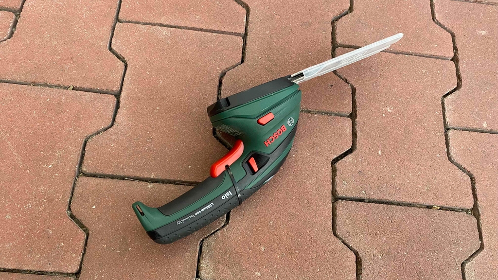 Getestete Akku-Grasschere liegt seitlich auf einem Steinboden.