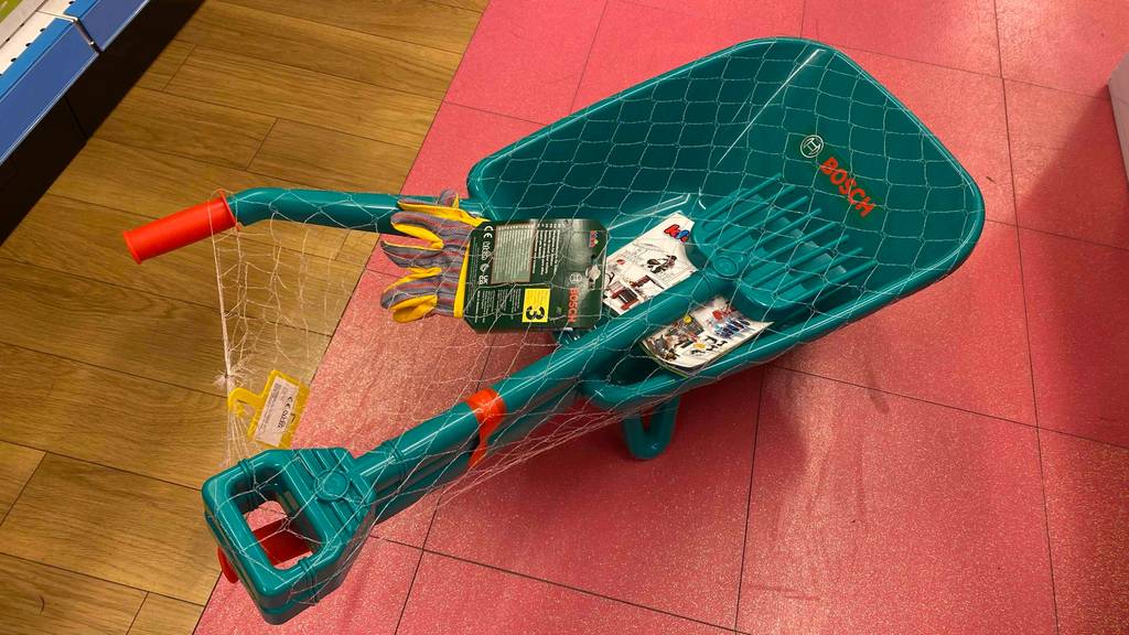 Eine getestete Kinderschubkarre von schräg oben auf einem roten Boden.