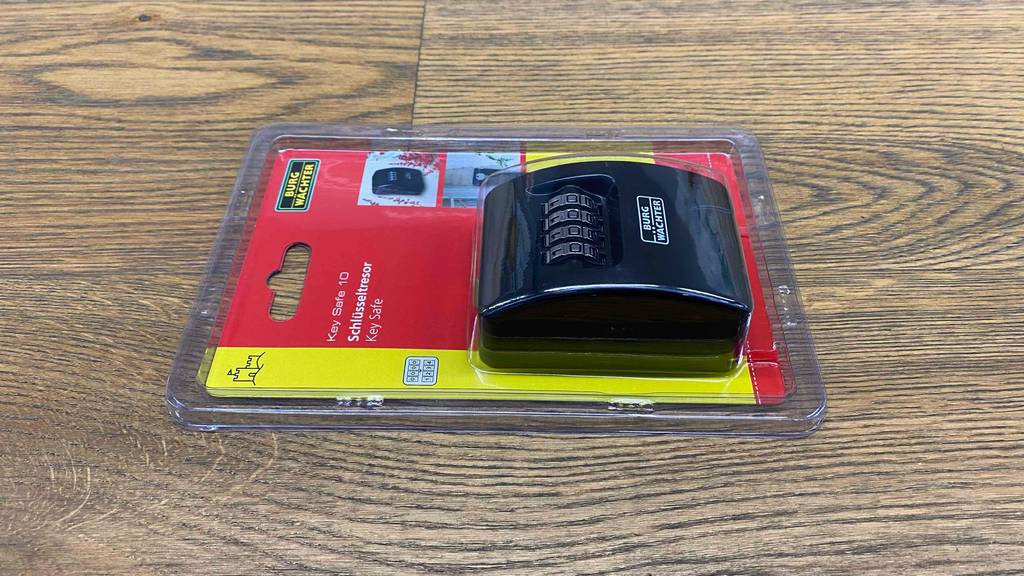 Schlüsseltresor getestet: Schlüsseltresor mit Zahlenschloss liegt in durchsichtiger Verpackung auf einer Holzfläche.