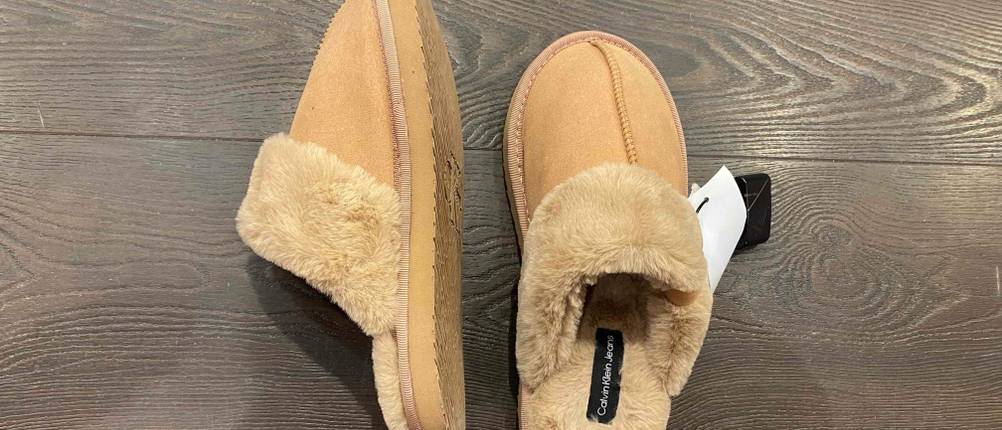 Lammfell-Hausschuhe im Test: ein Schuh gerade einer auf der Seite auf einem Holzboden, der anderen in Normalposition daneben platziert.