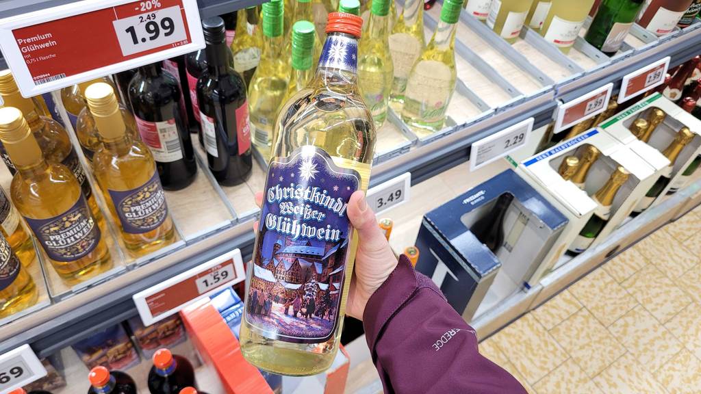 Eine Flasche getesteter weißer Glühwein wird in der Hand gehalten.