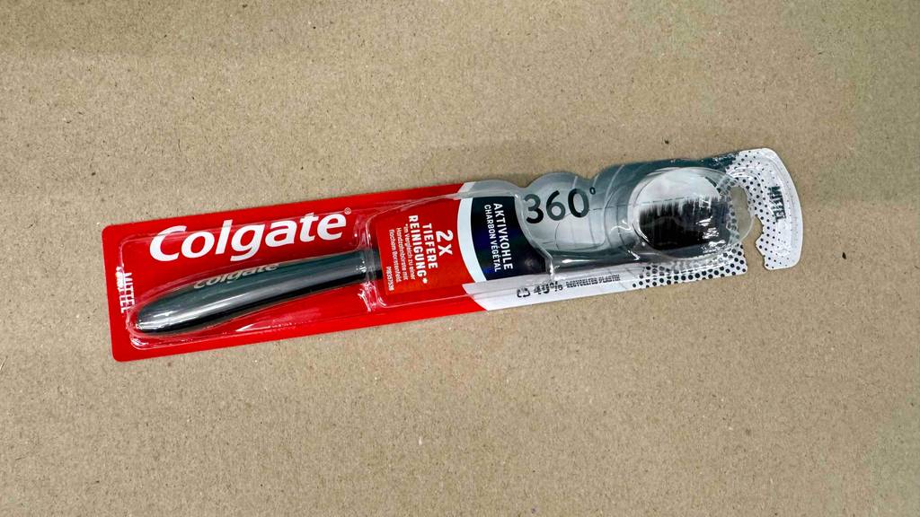 Aktivkohle-Zahnbürsten geteste: Ein Modell von Colgate liegt eingepackt auf einer beigefarbenen Oberfläche.