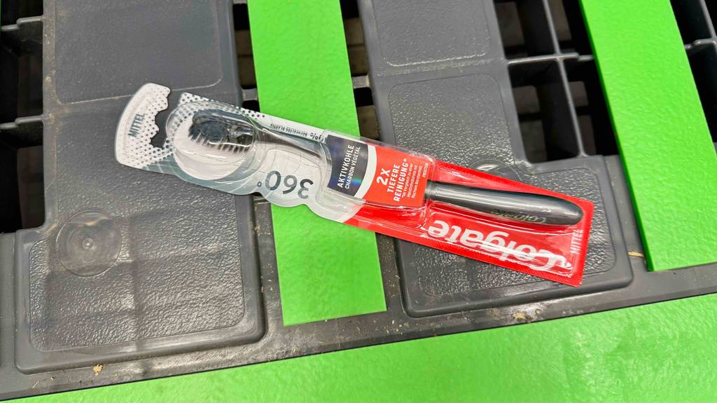 Im Test: Eine Aktivkohle-Zahnbürste von Colgate liegt auf einem grün-grauen Kunststoffkorb.