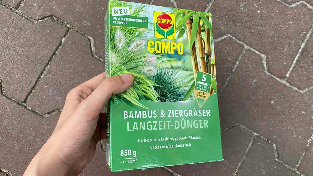 Bambusdünger im Test: Eine Hand hält eine Packung vor einen dunklen Untergrund