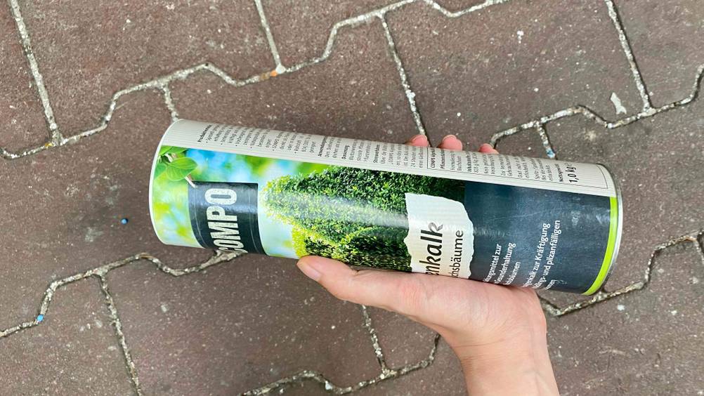 Eine Hand hält eine Dose des getesteten Algenkalks schräg vor einen Steinboden.
