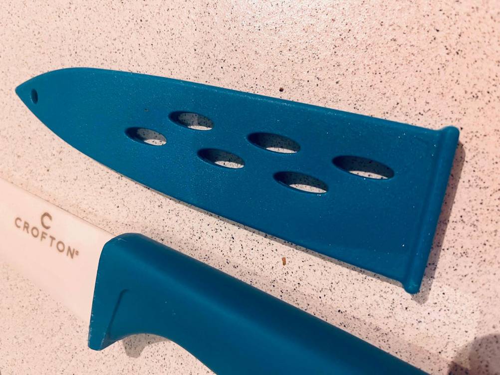 Keramikmesser getestet: blaue Schutzkappe liegt neben Keramikmesser mit blauem Griff.