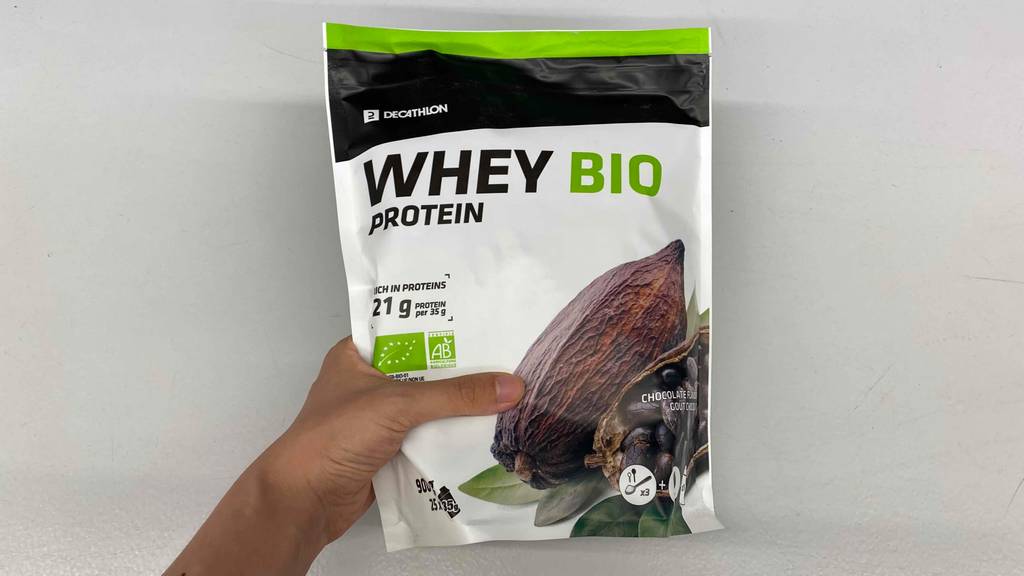 Bio-Whey-Protein im Test: Eine Hand hält eine Packung Protein vor eine helle Wand