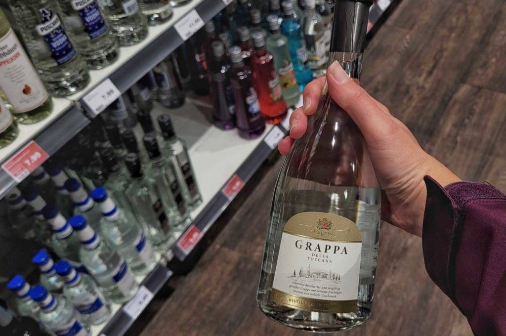 Grappa-Test: eine Flasche Grappa wird in der Hand vor einem Regal gehalten.