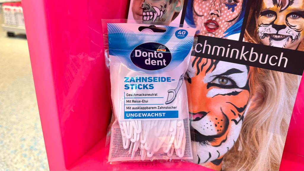 Eine Packung der getesteten Zahnseide-Sticks der Marke Donto-Dent steht vor einem Schminkbuch.