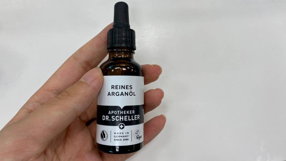Arganöl-Creme im Test: Eine Hand hält ein Fläschche vor eine helle Oberfläche