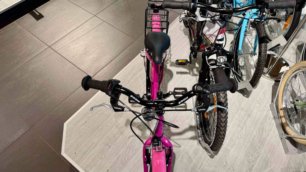 Ansicht von oben auf das getestete Mädchenfahrrad 20 Zoll in Pink, das neben anderen Fahrrädern auf einem Podest im Geschäft steht.