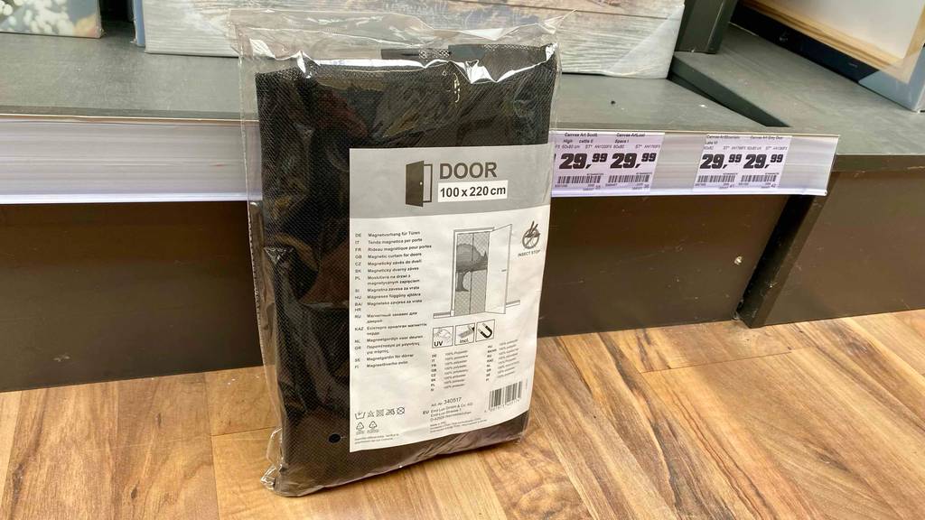 Fliegengittertüre-Test: eine schwarze Fliegengittertüre mit Maßen von 100 x 200 cm ist in der Verpackung an ein Regal angelehnt.