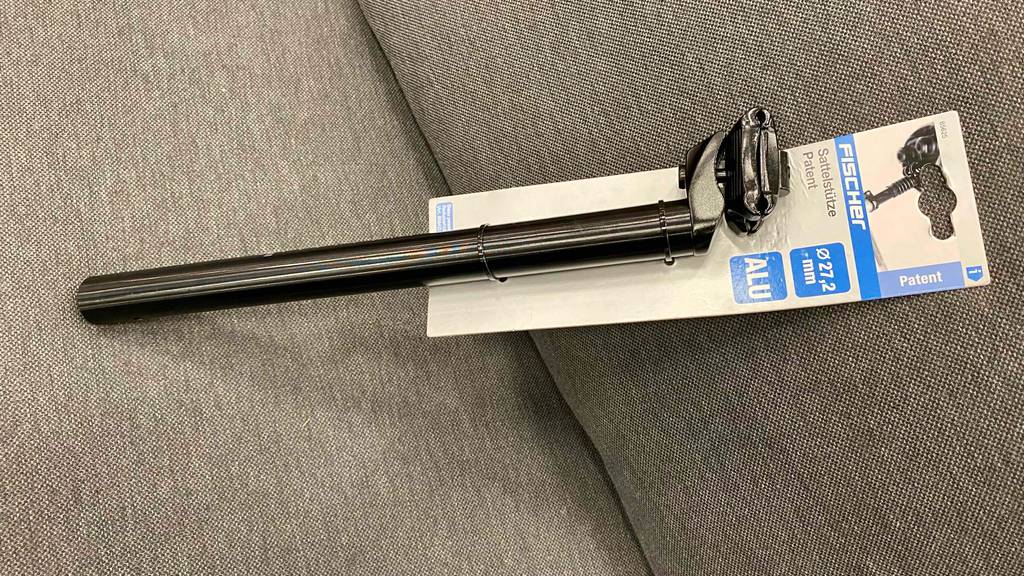 Sattelstütze-Test: eine schwarze Sattelstütze an Verpackung befestigt, ist auf einem grauen Sitzplatz platziert.