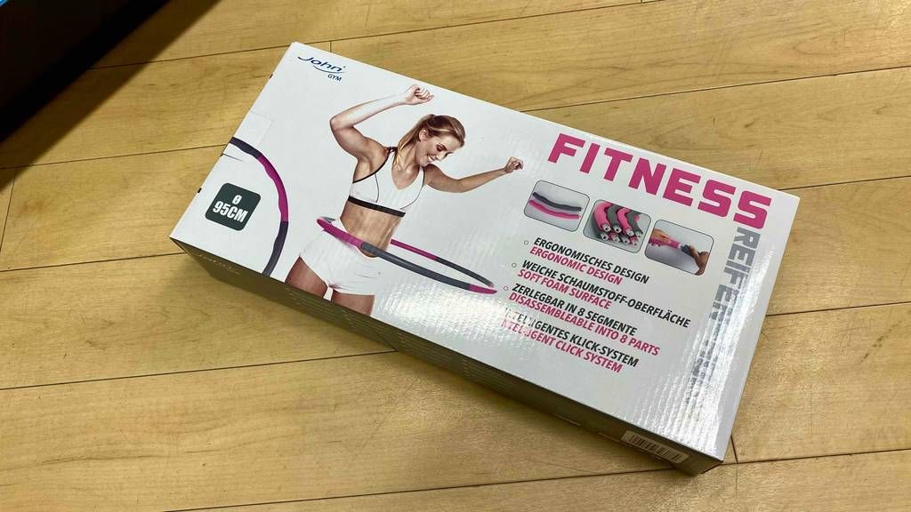 Im Test: Auf einem Holzboden liegt ein verpackter Hula Hoop Reifen.