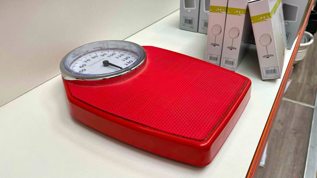 eine rote, getestete analoge-Personenwaage ist in einem Regal platziert.