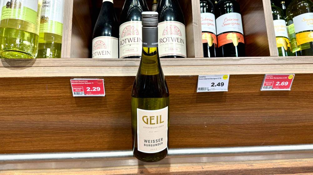 Eine Flasche getesteter Weißburgunder ist vor einem Getränkeregal ausgestellt.