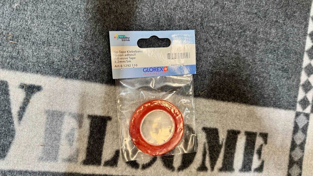 Das getestete Klebeband befindet sich in einer transparenten Tüte, die auf einem Teppich liegt.