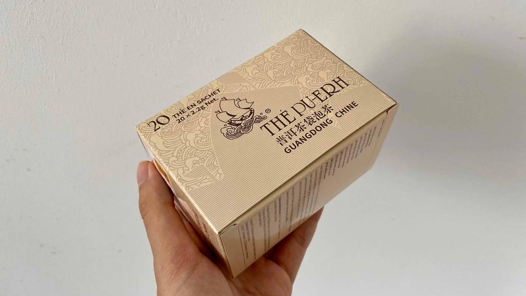 Pu-Erh-Tee im Test: Eine Hand hält eine Packung Tee vor einen hellen Hintergrund