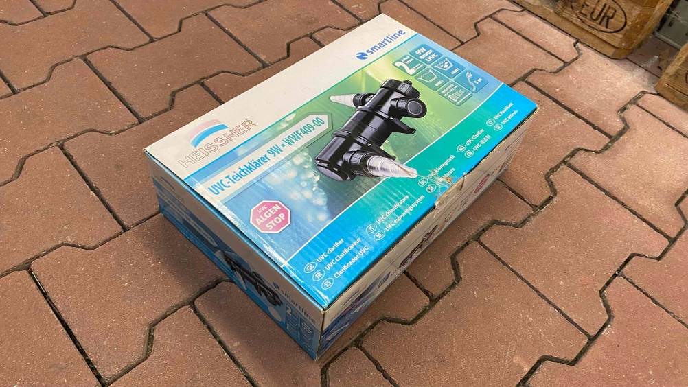 Ein getesteter UVC-Teichklärer in Verpackung liegt auf einer Steinfläche.
