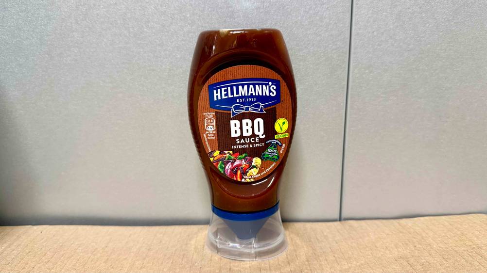 Die getestete Grillsauce die sich in einer Überkopftube befindet steht vor einer Wand.