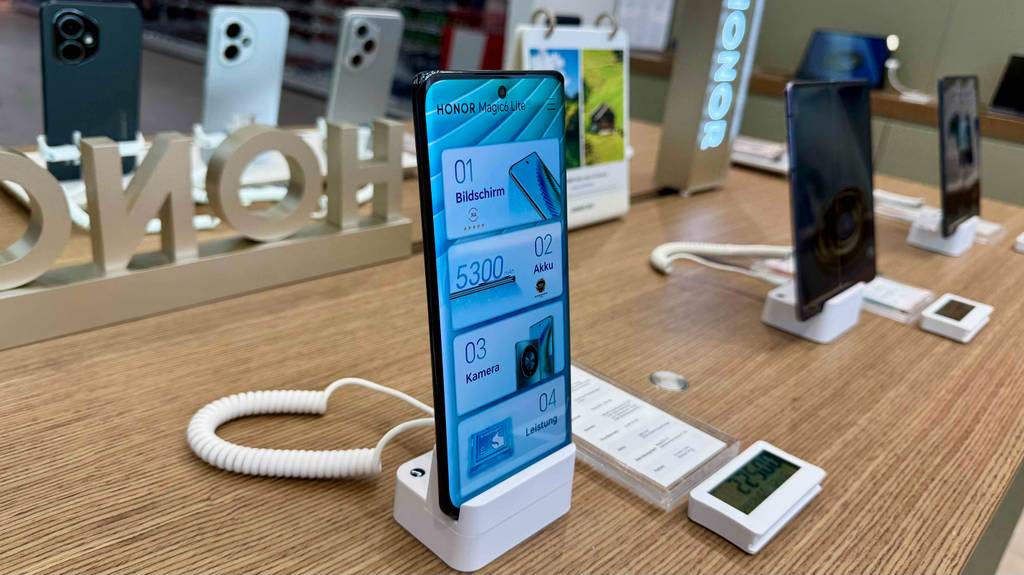 Das getestete Smartphone bis 250 Euro von der Seite betrachtet, mit Fokus auf das eingeschaltete Display, steht in einem Verkaufsbereich.